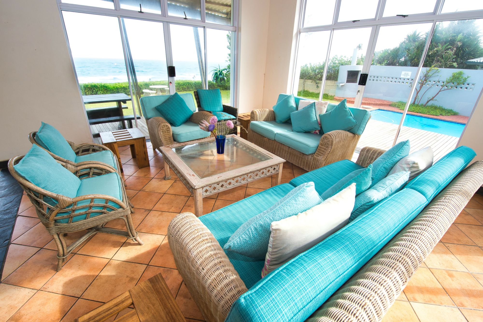 Rascal’s Rest - lounge area, wooden and teal cushioned furniture. Looking out onto the ocean