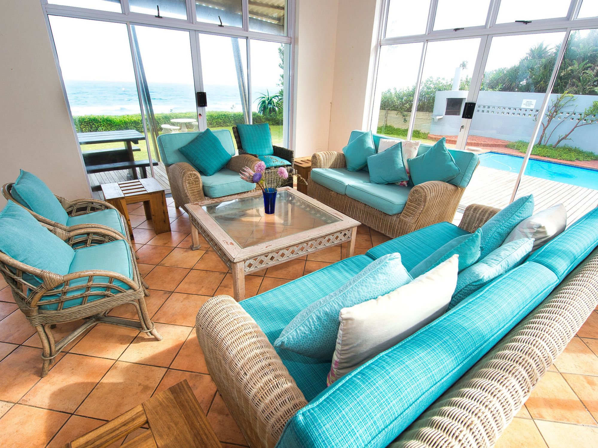 Rascal’s Rest - lounge area, wooden and teal cushioned furniture. Looking out onto the ocean.