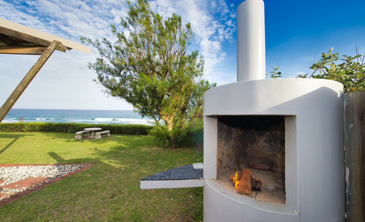 The outside fireplace is displayed to the right of the image, with the ocean, front lawn, and cemented garden furniture towards the left