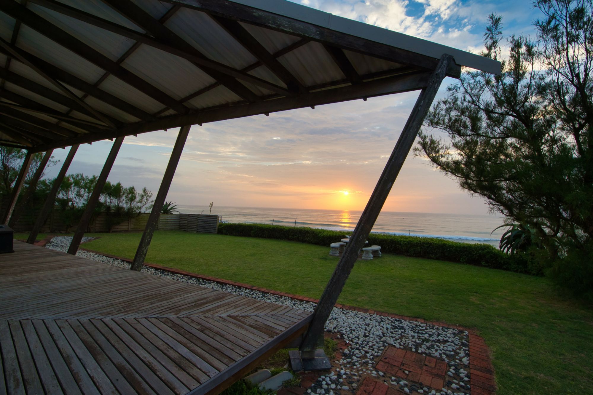 Angled sunset over sea view from holiday home patio right side, front lawn is visible, with cemented garden furniture